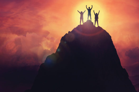Three people on a mountain top at sunset.