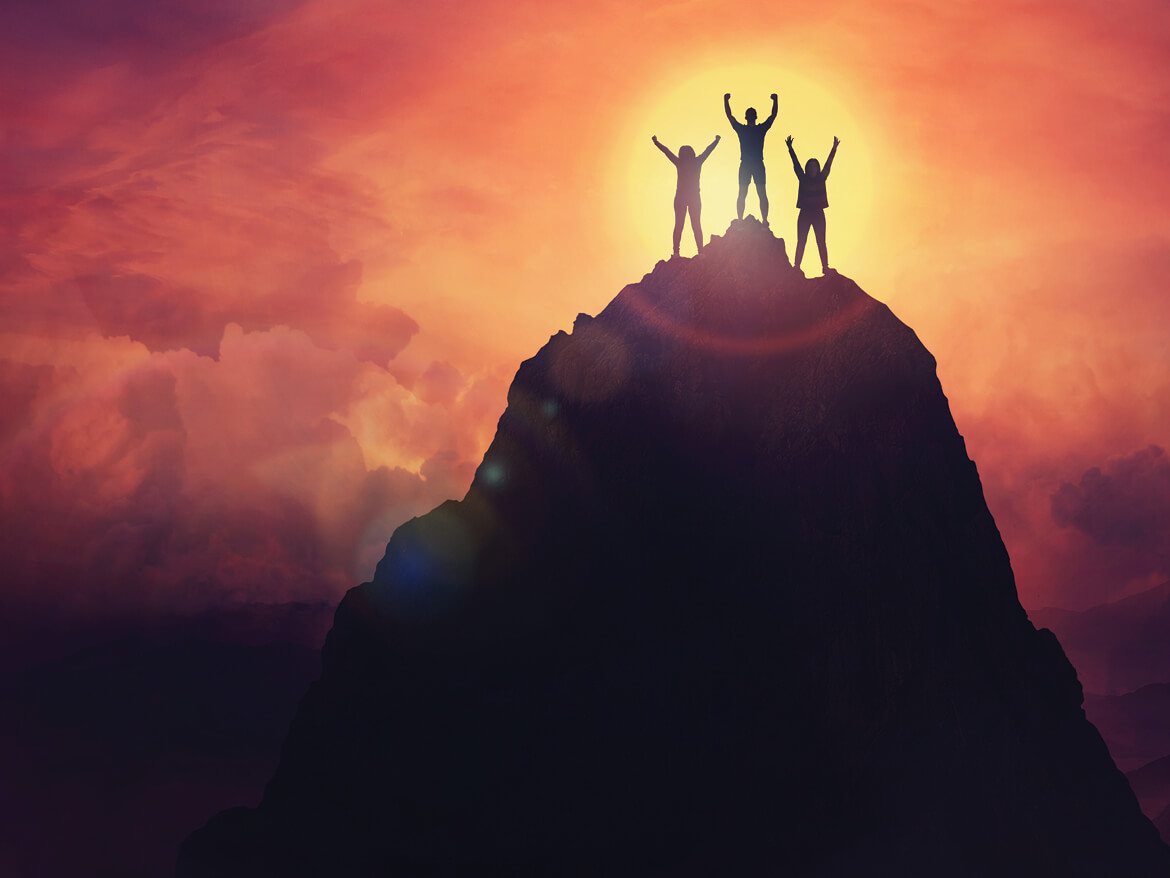 Three people on a mountain top at sunset.