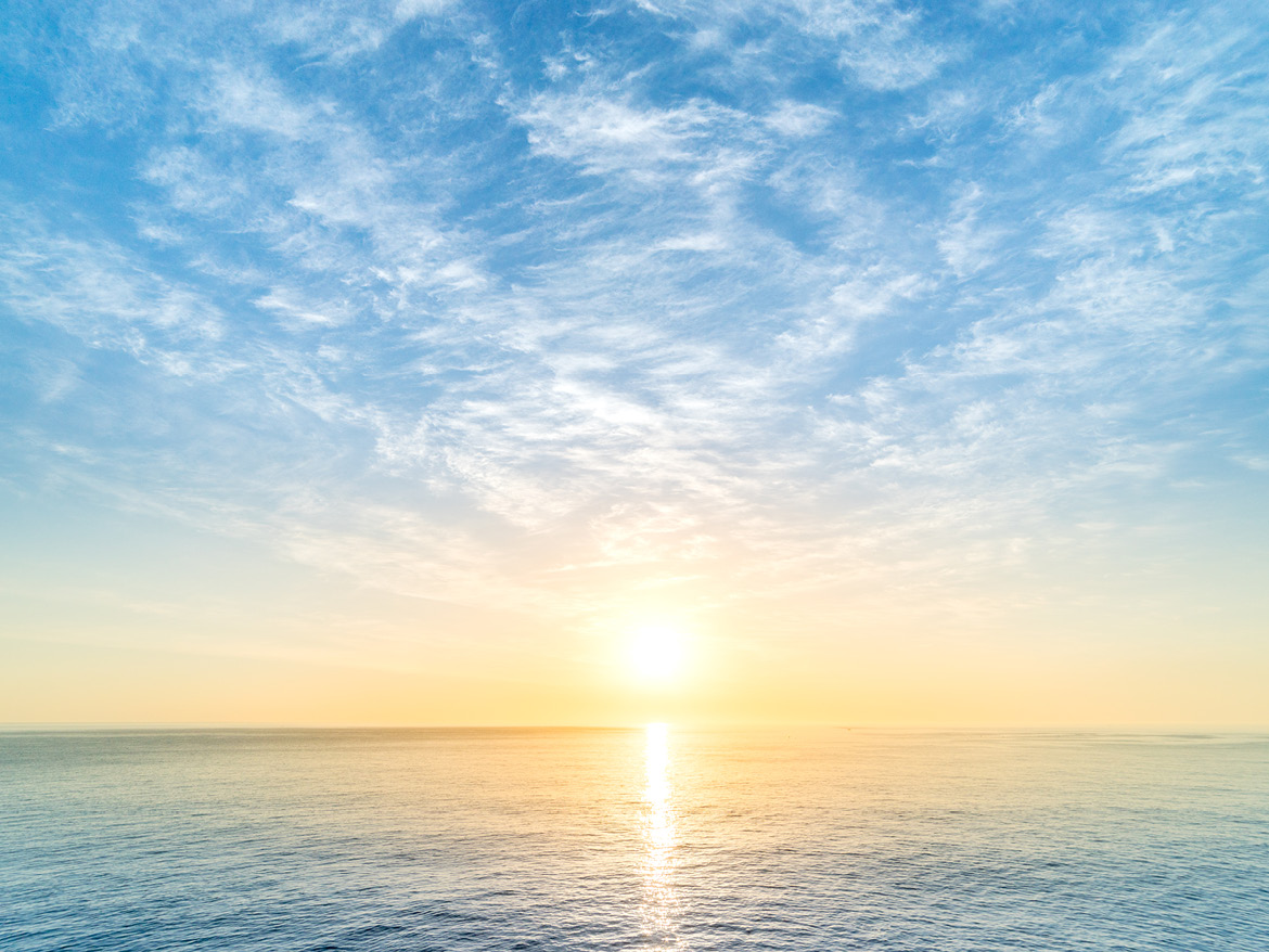 A view of the sky, sun and sea, with sunlight reflected on the water.